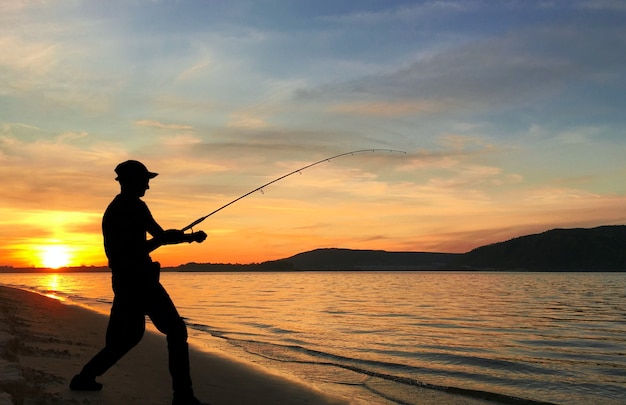 Young man fishing on a lake at sunset