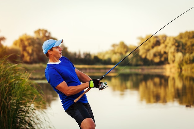 Young man fishing on river at sunset