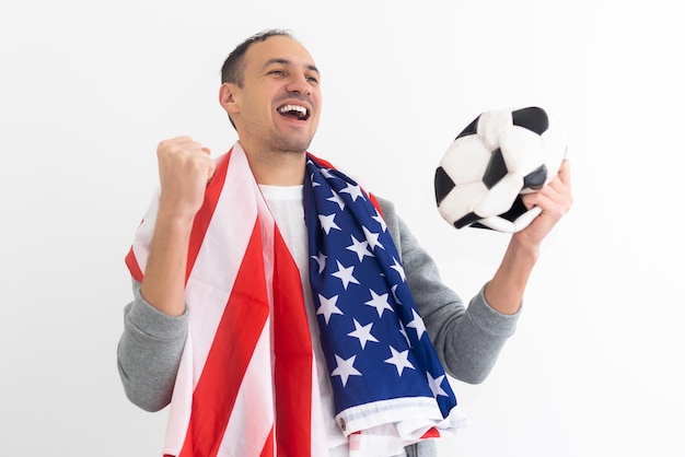 Young man football fan in shirt support team with soccer ball sit sofa home watch tv use mobile cell phone blank screen workspace area show thumb up isolated on orange background People sport concept.