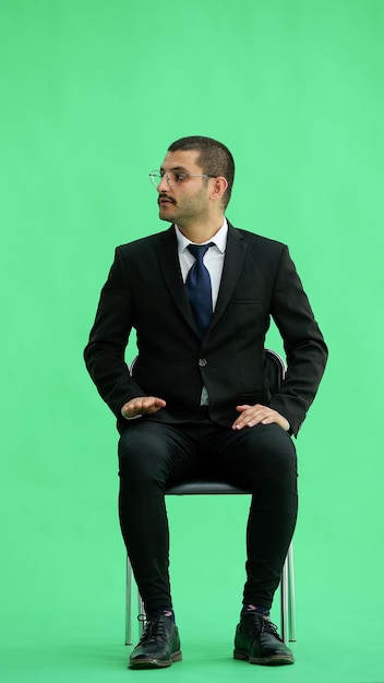 Photo young man in full growth isolated on a green background sitting on a chair