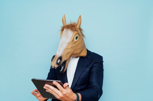 Young man in funny horse mask works with a portable tablet.