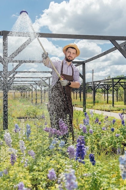 Young man gardener take care of plants by watering them in garden center