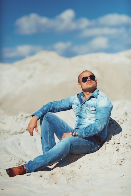 Young man in glasses lies in jeans clothes on the sand in Dubai