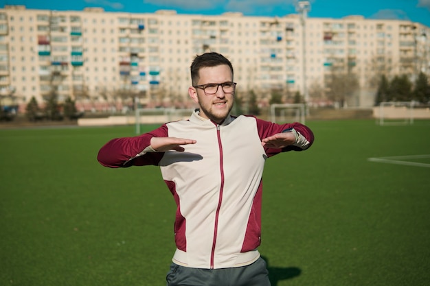 Young man in glasses stretching on a stadium