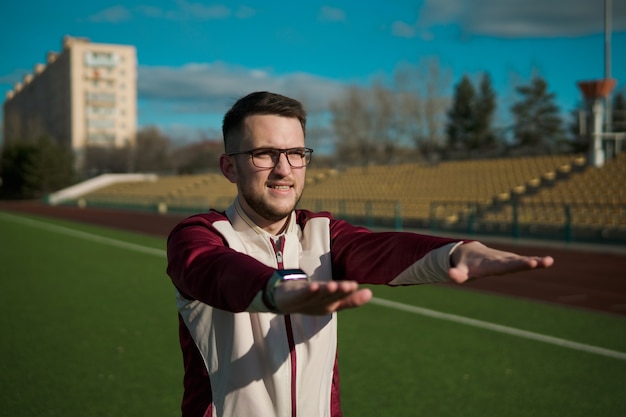 Young man in glasses stretching on a stadium