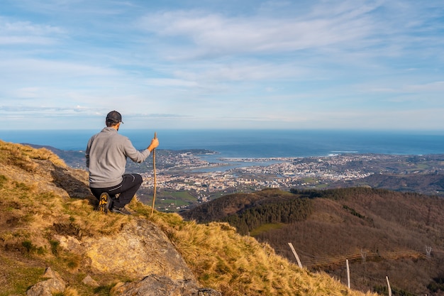 A young man in a gray sweater looking at the views of the towns of Hondarribia and Hendaya from the mountains of Aiako Harria or PeÃ±as de Aya, GuipÃºzcoa