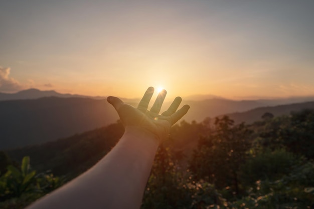 Young man hand reaching for the mountains during sunset and beautiful landscape