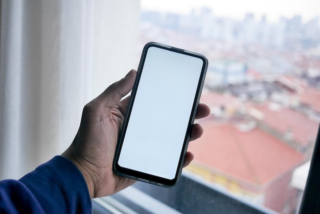 Young man hand using smart phone with green screen against city buildings