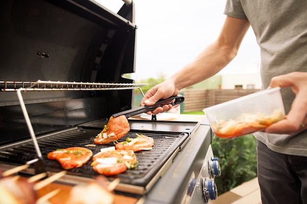 Young man hands turning the meat by fork on the gas grill