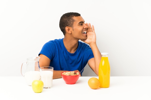 Young man having breakfast in a table shouting with mouth wide open