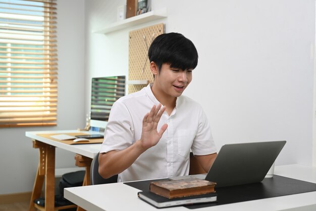 Young man having video call on laptop computer while sitting in home office.