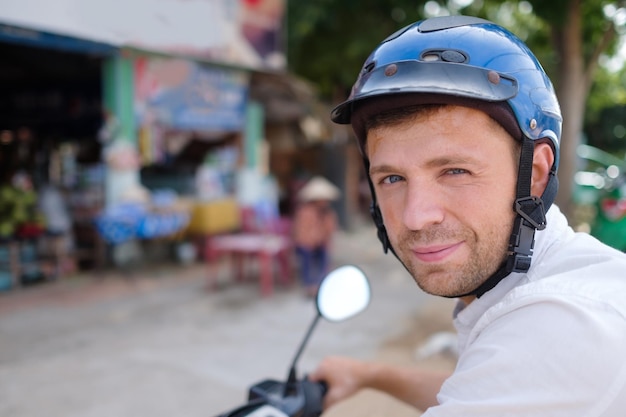 Young man in a helmet stays on a road of Asia watching at the camera