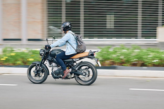 Young man in helmet with backpack riding fast on motorcycle along city roads