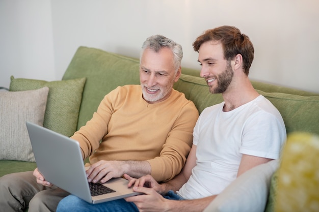 Young man and his dad watching something online and looking involved