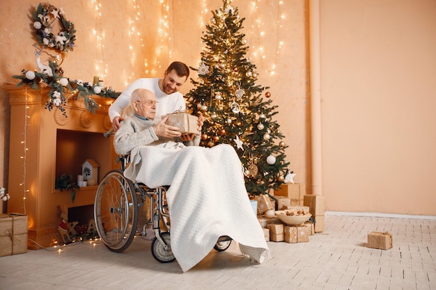 Young man and his old father on a wheelchair sitting near Christmas tree