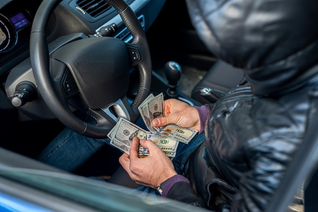 Young man in his own cool car calculates the salary in dollar bills Business concept The concept of a driver in a car