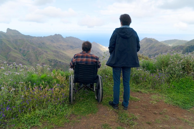 Young man and his wife in wheelchair travelling together in mountains