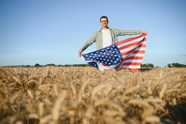 Young man holding American flag standing in wheat field