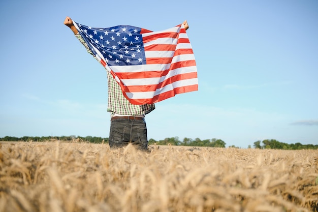 Young man holding American flag standing in wheat field