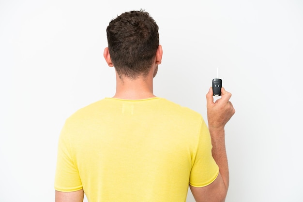 Young man holding car keys isolated on white background in back position