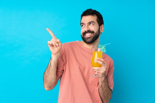 Young man over holding a cocktail over isolated blue wall pointing with the index finger a great idea