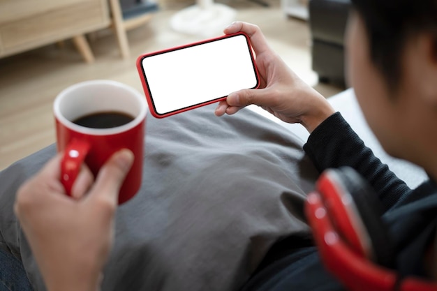 Young man holding coffee cup and using mobile phone in living room