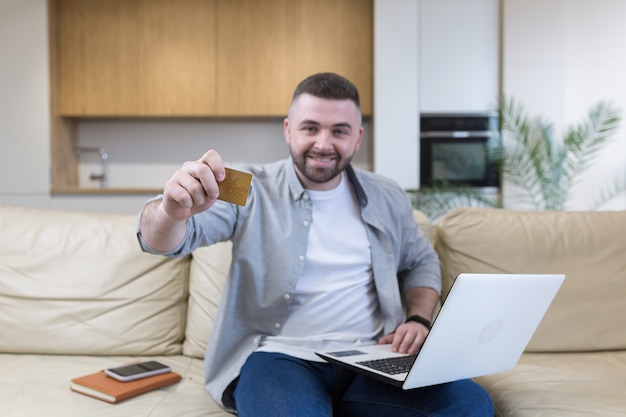  Young man holding credit card and using phone at home office