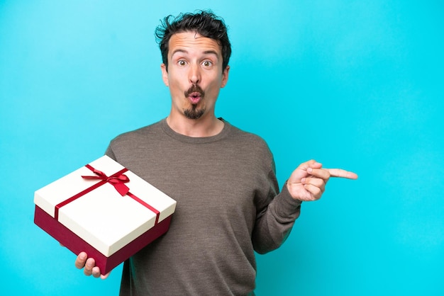 Young man holding a gift surprised and pointing side