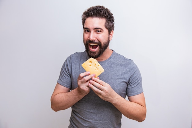 Young man holding a grater and a piece of cheese in his hand on gray background. man will grate the cheese