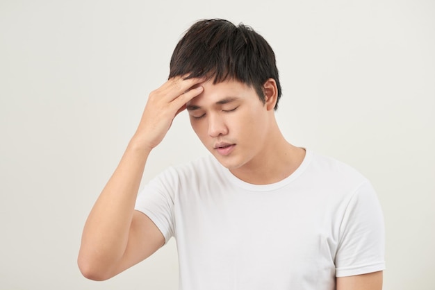 A young man holding his head with his hand looks tired with a headache isolated on a white background