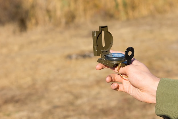 Young man holding a magnetic compass as he stands outdoors in the countryside using it for navigation and to find his geographic location