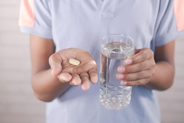 Young man holding pills and glass of water with copy space