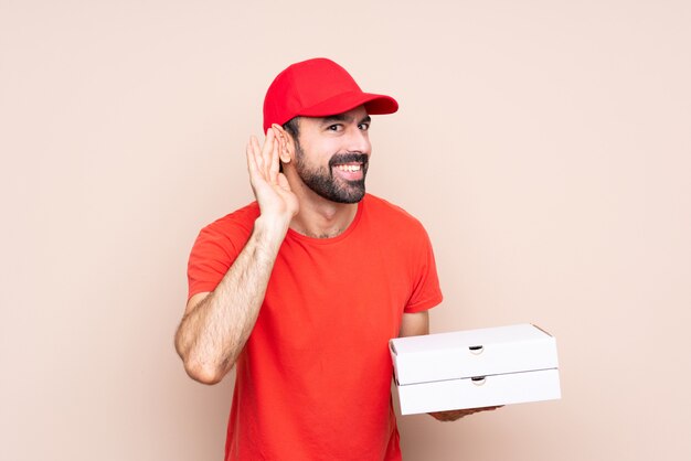 Young man holding a pizza listening to something by putting hand on the ear