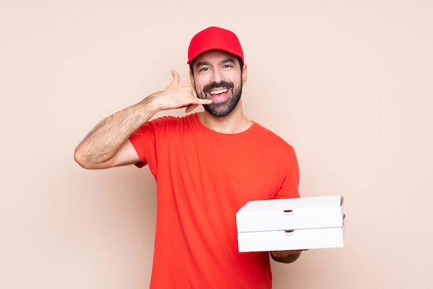 Young man holding a pizza making phone gesture. Call me back sign