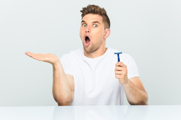 Young man holding a razor blade impressed holding copy space on palm.