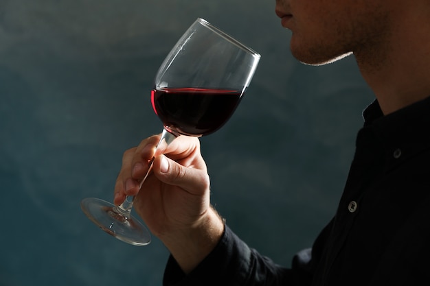 Young man holding red wine glass against dark background, space for text