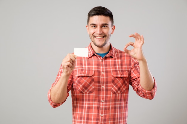 Young man holding and showing blank business card isolated on gray background