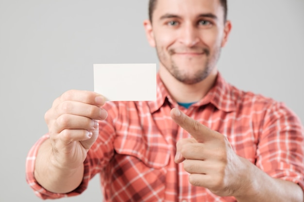 Young man holding and showing blank business card isolated on gray background