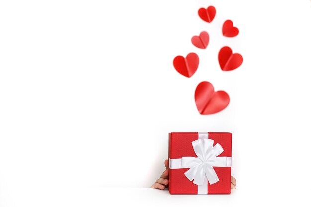 A young man holding a small present box with red hearts on a white background