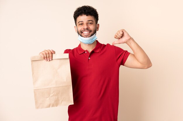 Young man holding a takeaway food bag proud and self-satisfied