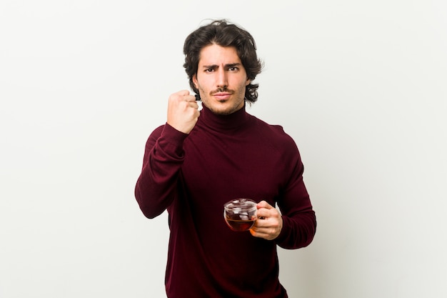 Young man holding a tea cup showing fist with an aggressive facial expression.