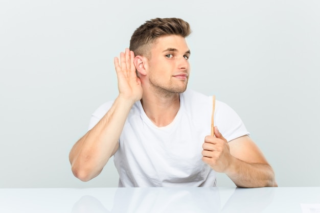 Photo young man holding a toothbrush trying to listening a gossip.