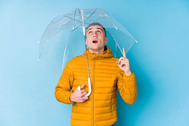 Young man holding an umbrella pointing upside with opened mouth