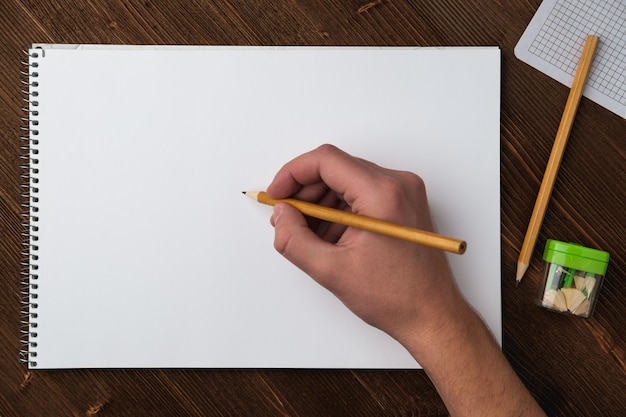 A young man holds a pencil in his hand over a sketchbook with white sheets