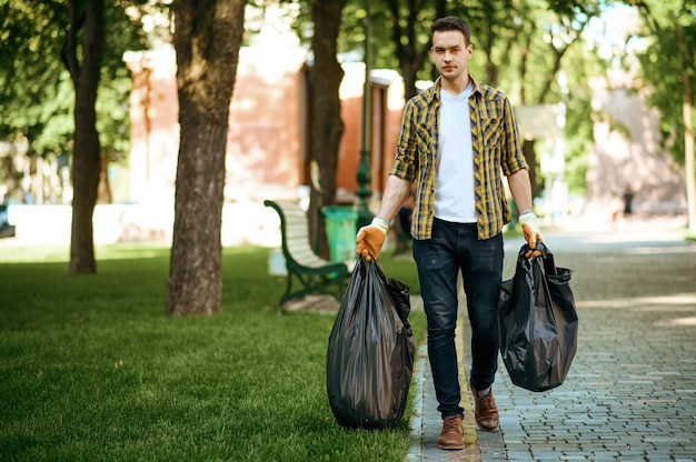 Young man holds plastic trash bags in park, volunteering