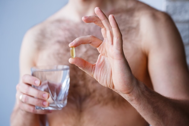 A young man holds vitamins and a glass of water in his hands. Immunity pills