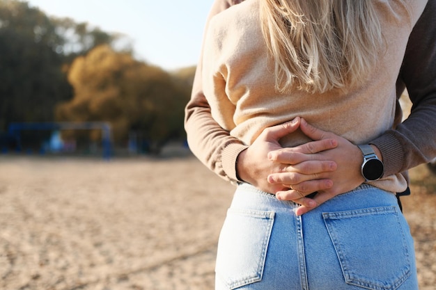 A young man hugs a girl in jeans and a sweater around the waist fingers crossed on her back Closeup of hands