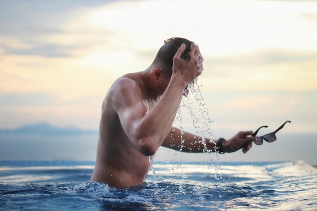 Young man in the infinity pool on a background of beautiful sunset