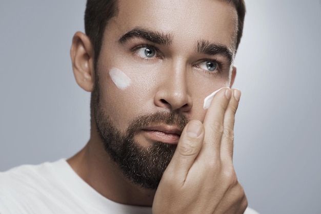 Young man is applying moisturizing cream on his face