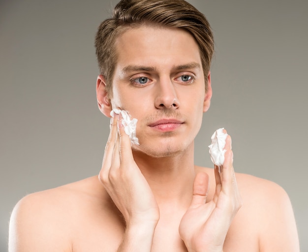 Young man is applying shaving cream to his face.